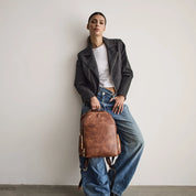 Person holding a brown leather backpack against a plain background