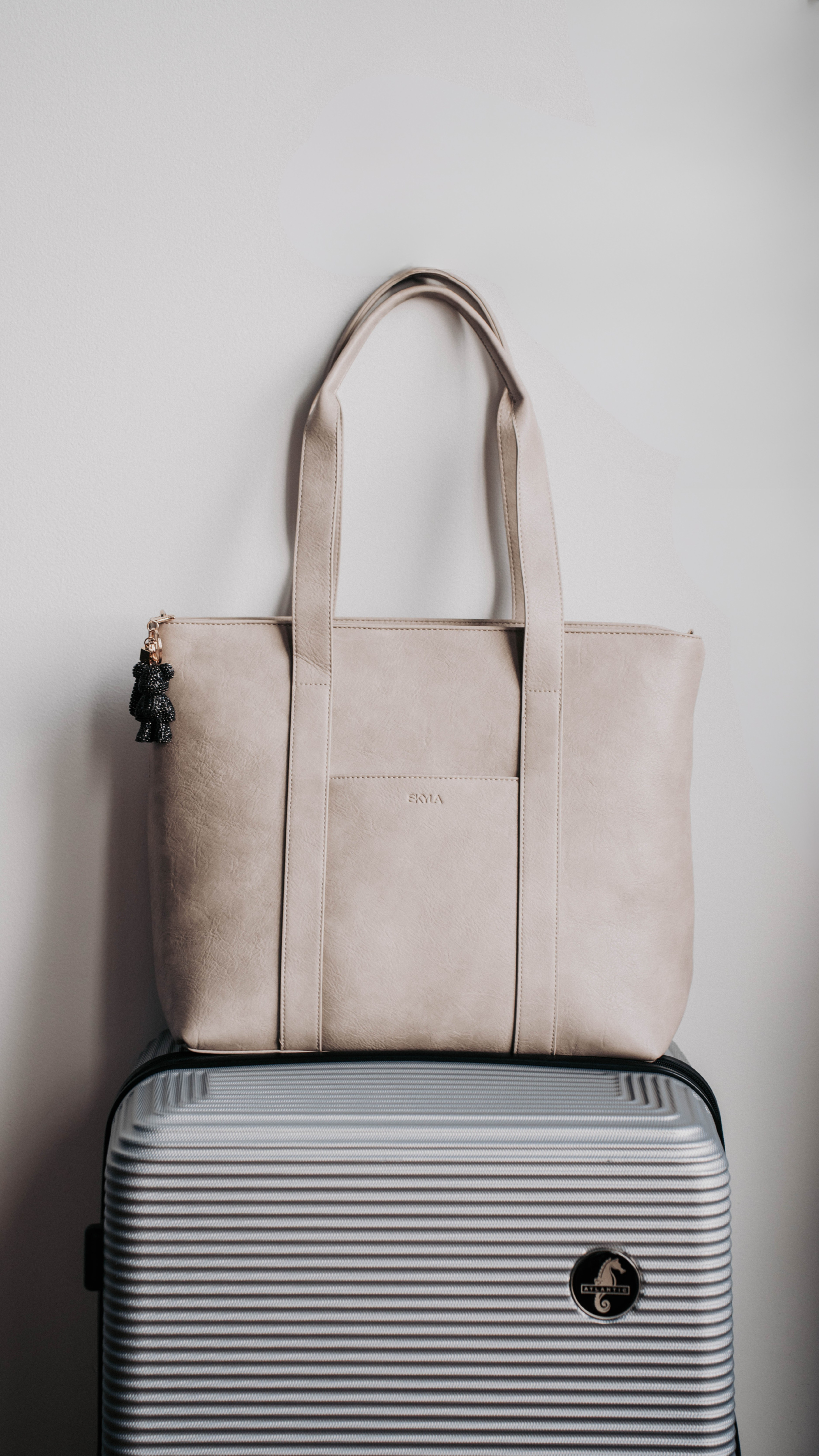 Beige tote bag on a striped suitcase against a plain background